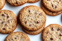 Crunchy chocolate chip cookies with chopped nuts arranged on white background. Close-up view shows golden brown texture and scattered chocolate pieces throughout.