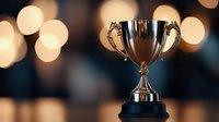 Shiny silver trophy cup on dark background with soft bokeh lights creating festive atmosphere. Award symbolizes achievement, victory and success in competition.