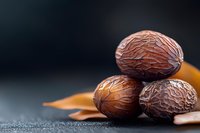 Whole nutmeg spices with natural brown shells stacked on dark surface with warm lighting for culinary cooking and baking ingredients.