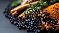 Aromatic spices and herbs arrangement with black peppercorns, star anise, cinnamon sticks, rosemary, and vibrant orange curry powder on dark background, macro shot.