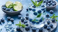 Fresh blueberry mojito cocktail with lime, mint leaves and ice cubes. Refreshing summer drink garnished with berries on blue background.