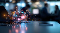 Glowing orange and blue particles emerging from smartphone screen on dark table, creating magical light effect in blurred office environment.