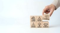 Hand placing wooden cube with collaboration icon among blocks showing teamwork, structure, innovation, and partnerships concepts on white background.