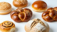 Assorted fresh baked bread rolls and buns with sesame seeds on white background for bakery menu design and food photography projects.