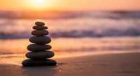 Balanced stone cairn on sandy beach at golden sunset with soft ocean waves creating peaceful meditation and mindfulness atmosphere for wellness concepts.