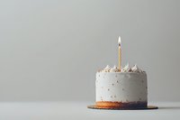 White frosted birthday cake with single lit candle and gold sprinkles on minimal gray background, styled for modern celebration photography.