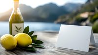 Fresh lemons and olive oil bottle on wooden table against blurred Mediterranean coastal landscape, blank white greeting card for copy space. Sunny outdoor setting.
