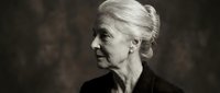 Elegant senior Caucasian woman in profile with silver hair in updo wearing black clothing against dark textured background in monochrome portrait style.