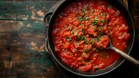Fresh homemade tomato sauce simmering in rustic cast iron pan with herbs and spices on weathered wooden table, traditional Italian cooking preparation.