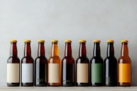 Craft beer bottles with blank labels arranged in row on gray concrete shelf, showing variety of beer colors from light to dark amber and stout. Mockup for branding.