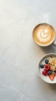 Overhead shot of cappuccino with latte art and bowl of granola with fresh berries on marble surface, ideal for breakfast and cafe content.
