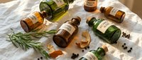 Collection of essential oil bottles with natural herbs and spices on white linen background for aromatherapy and wellness products.