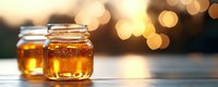 Golden honey in glass jars on wooden surface with warm bokeh lights in background, natural organic sweetener glowing in sunlight, food photography.