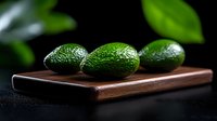 Fresh ripe avocados on wooden cutting board against dark background with green leaves. Natural food photography for restaurant menu and cooking blogs.
