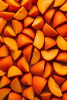 Fresh orange persimmon slices arranged in a vibrant pattern on dark background, showing juicy fruit texture and natural color for food photography and design.