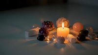 Burning candle surrounded by healing crystals and gemstones creating warm ambient lighting for meditation and spiritual wellness practices.