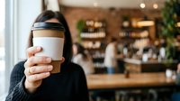 Woman holding takeaway coffee cup in cafe environment, suitable for beverage, lifestyle, and hospitality marketing materials.