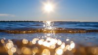 Sparkling sunlight creates magical bokeh effect on ocean waves with golden reflections during sunset, low angle view capturing water surface and bright blue sky.