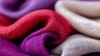 Luxurious silk fabric waves in red, purple and white colors creating elegant folds and curves. Textured textile material with soft focus macro photography shows fine weave details.