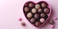 Assorted chocolate truffles and pralines in pink heart shaped box on pastel background with scattered candy hearts, romantic holiday confectionery setting.