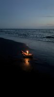 Small wooden boat with glowing lantern on twilight beach shore creates magical atmosphere as waves gently wash sand under dusky evening sky.