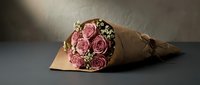 Elegant pink rose bouquet wrapped in brown kraft paper with baby's breath flowers on dark surface for romantic gifts and special occasions.