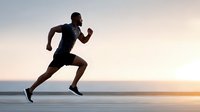 Athletic young man running at sunset on waterfront promenade with ocean view. Fitness motivation and healthy lifestyle concept for sports marketing.