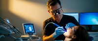 Male dentist examining female patient in modern dental office with digital equipment and blue lighting for professional healthcare treatment.