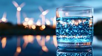 Glass of sparkling water with wind turbines silhouettes in background at dusk, bokeh lights reflecting on surface creating magical atmosphere for sustainability concept.