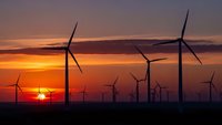 Wind turbines silhouetted against dramatic sunset sky with orange and purple clouds. Renewable energy farm generating clean electricity at dusk.