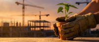 Worker in work gloves holding seedling plant at construction site during sunset, symbolizing sustainable development and environmental responsibility in building industry.