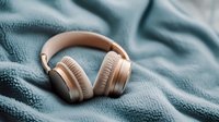Rose gold wireless headphones on soft blue textured blanket, showcasing premium audio equipment for lifestyle and technology marketing.
