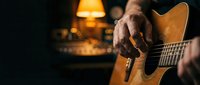 Close-up of male hands playing acoustic guitar in warm cozy living room with lamp light creating intimate musical atmosphere for relaxation and creativity.