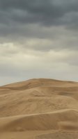 Vast desert sand dunes with carved symbols and markings under dramatic overcast sky, suitable for travel, nature, and environmental design projects.
