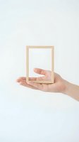 Hand holding wooden picture frame creating optical illusion on white background isolated for creative design projects and conceptual artwork.