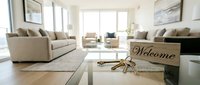 Modern bright living room with welcome sign and keys on glass table, new home ownership concept, real estate and property rental.