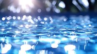 Tranquil blue water surface with sunlight creating magical bokeh effect and gentle ripples, close-up view showing liquid texture and natural light reflections.