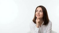 Thoughtful young Caucasian businesswoman in white shirt looking up with hand on chin, contemplating ideas against clean background for corporate use.