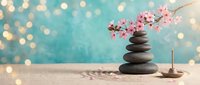 Zen spa composition with balanced stones, cherry blossom branch and incense on turquoise bokeh background for meditation and wellness concepts.
