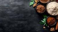 Various types of flour and cocoa powder in wooden bowls on dark stone background with walnuts, cinnamon sticks and fresh parsley leaves, copy space.