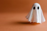 Playful white ghost decoration with black eyes floating against orange background, creating spooky Halloween atmosphere. Simple minimalist design for seasonal decor.