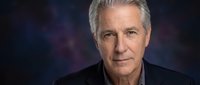 Mature man with gray hair and light complexion wearing dark casual shirt against blurred blue and purple background, suitable for corporate portraits, business profiles, and professional headshots.