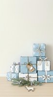 Stacked gift boxes in blue and white with snowflake patterns, tied with ribbons and bows, arranged on wooden surface with evergreen branches and decorative reindeer ornament for holiday celebrations.