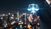 Businessman hand touching glowing justice scales icon with city lights background. Legal technology concept for law firms and judicial services.