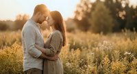 Young couple embracing intimately in golden sunset field, romantic moment with warm light, love and connection in natural outdoor setting.