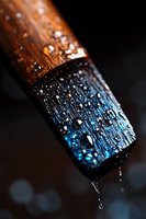 Macro shot of wet paintbrush with water droplets against dark background, showing wooden handle and blue bristles with dramatic lighting and bokeh effect.