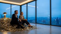 Wealthy business couple sitting on pile of money in luxury penthouse office with panoramic city skyline view through floor-to-ceiling windows at dusk.