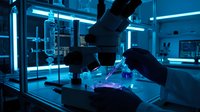 Scientist conducting laboratory research with microscope and glowing samples in modern lab environment with neon blue lighting for scientific study.