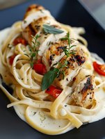 Grilled chicken breast slices with herbs served over creamy fettuccine pasta with cherry tomatoes and fresh basil for gourmet Italian cuisine dining.