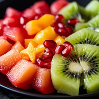 Fresh tropical fruit platter with watermelon, mango, pomegranate seeds and kiwi slices arranged on black plate, macro food photography for healthy eating.